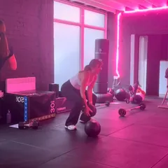 A class mid-workout with medicine balls in the pink-lit gym