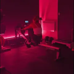 A member on the rowing machine under pink lights at the gym